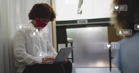 Seated man typing on laptop causing social icons growing around him, red mask Stock Footage 329506189