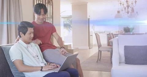 Seated man typing on laptop on couch after teenager leaning in, sharing tech Stock Footage 322702588