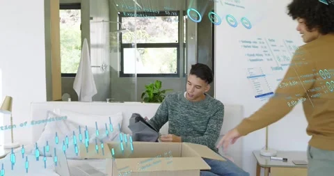 Seated man unpacking box pulling gray sweater as standing man sorting notes tech Stock Footage 323335047
