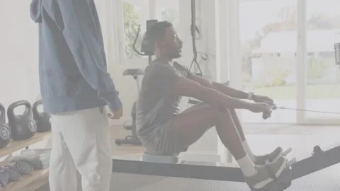 Seated rower starting strokes on slide machine while coach supervising training Stock Footage 332704981