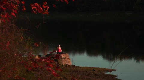 Seated side bend yoga progression on rock near lake Stock Footage 44120527