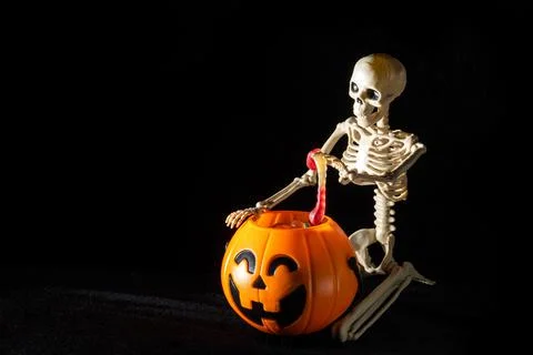 A seated skeleton pulls out of a bucket in the shape of a pumpkin candy on a  Stock Photos