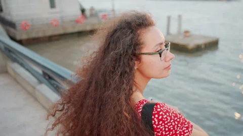 Seated young lady on bridge lost in peaceful thought during evening. Candid 库存影片 338283322
