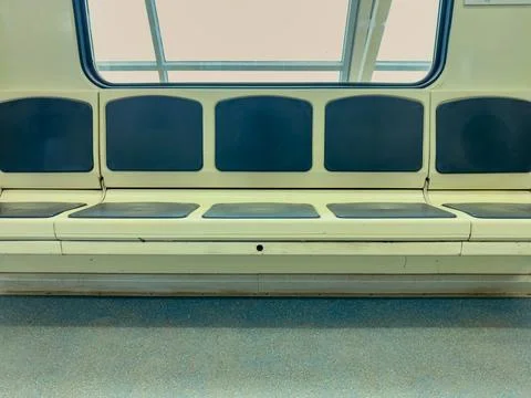 Seating area in a subway train shows several empty seats with a bright window Stock Photos