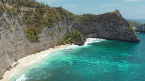 Secluded beach beneath towering cliffs, with turquoise waves crashing against Stock Footage 288255141