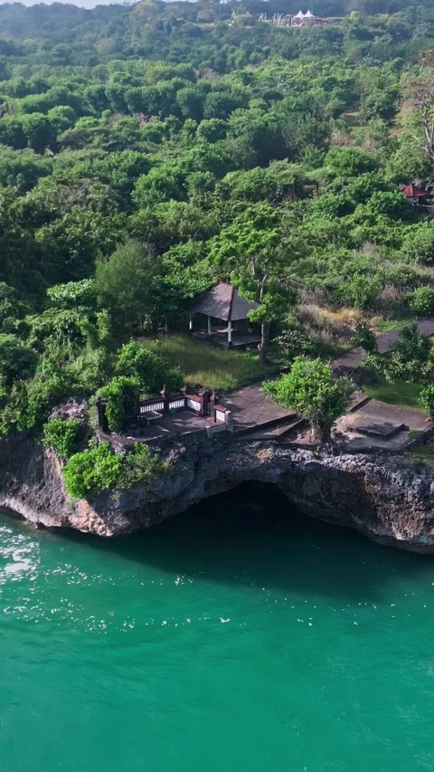 Secluded cliffside shrine surrounded by vibrant jungle and gentle waves Stock Footage 337136947