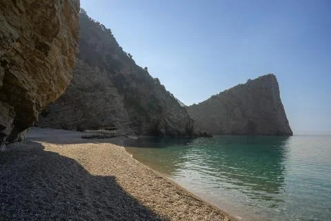 Secluded pebble beach surrounded by dramatic cliff formations and turquoise.. Stock Photos