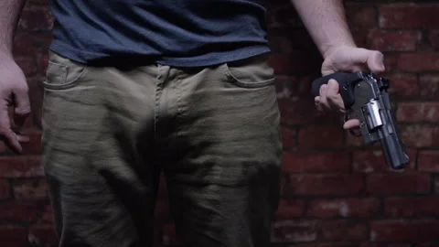 Second Amendment - Man lowers gun and cocks it in front of brick wall Stock Footage 300899826