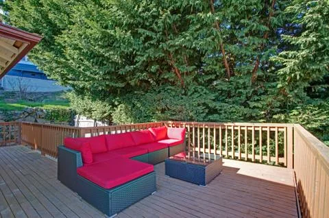Second floor deck features wicker outdoor sofa with red cushions. Stock Photos