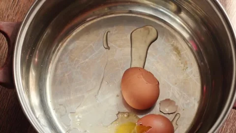 A second raw brown chicken egg falls into a metal cooking pot from above al.. Stock Footage 344112428