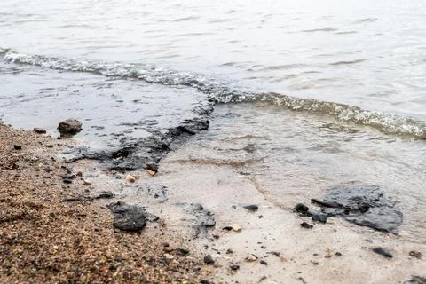 Section of beach polluted with black sludge, oil or tar, waves washing over.. Stock Photos