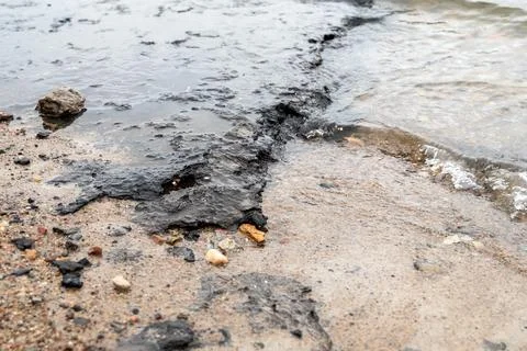 Section of beach polluted with black sludge, oil or tar, waves washing over.. Stock Photos