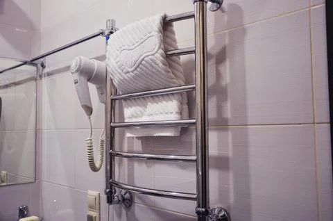 A section of a light-tiled bathroom. A stainless steel heated towel rail hang Fotos de archivo