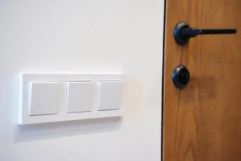 A section of a wall featuring three white light switches next to a wooden door Foto stock