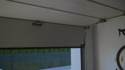 Sectional garage door is closing from inside with yard visible Stock Footage 334329549