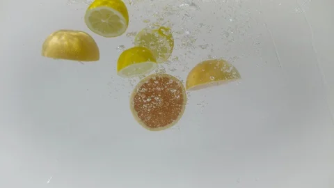 Sectioned grapefruits and lemons dropped into water, Ultra Slow Motion Stock Footage 86583282