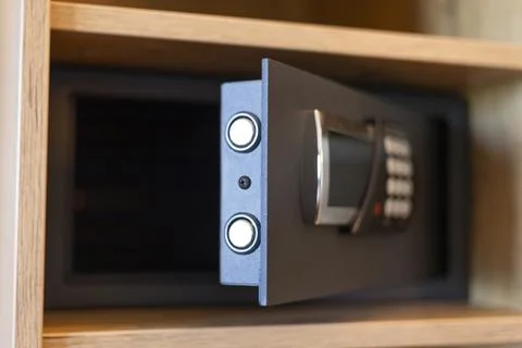 A secure safe with a digital keypad is partially open in a wooden cabinet. Th Stock Photos