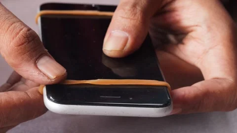 Securing a slightly lifted smartphone screen with a rubber band Stock Footage 345103485
