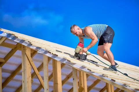 Securing timber battens over roofing underlay, worker uses nail gun while a.. Stock Photos