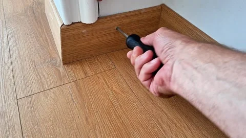 Securing a Wooden Baseboard with a Screwdriver During Floor Renovation Work Stock Footage 345703789