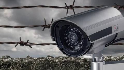 Security camera in front barbed wire fence stretched around prison walls Video stock 82512787