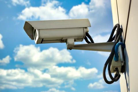 This is a security camera hanging on the wall of a building against a blue sky Stock Photos