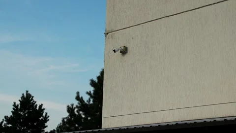 Security camera mounted on beige building wall against clear blue sky beside Stock Footage 346774091