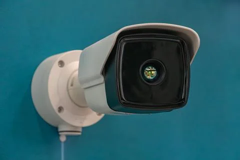Security camera mounted on a blue wall, white device with black lens cover,.. Stock Photos