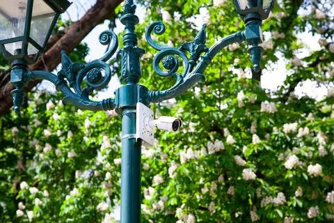 A security camera is mounted on a decorative lamp post in a park. The area is Stockfoto's