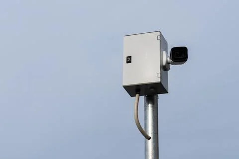 Security camera mounted on a metal pole against a clear sky Stock Photos