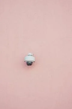 Security camera mounted on a pink wall in bright daylight Stock Photos