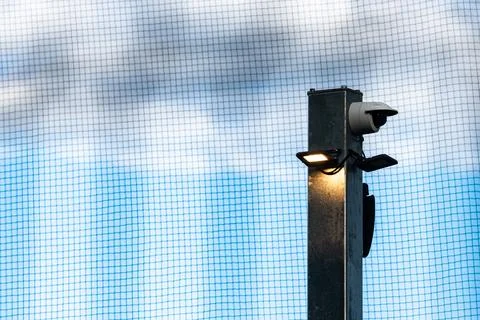 Security camera mounted on a pole under blue sky and netting Stock Photos
