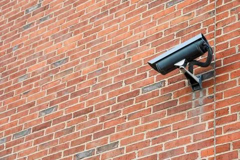 Security camera mounted on a red brick wall for surveillance and protection Stock Photos