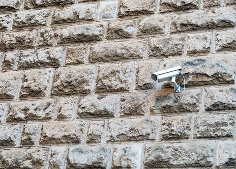 Security camera mounted on rough stone wall outdoors, surveillance system on 库存照片