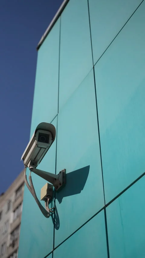Security camera mounted on turquoise exterior wall, tracking surroundings with Stock Footage 305497349