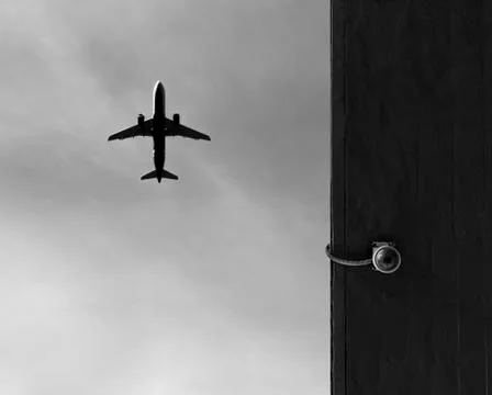 Security camera mounted on a wall with a plane above Stock Photos