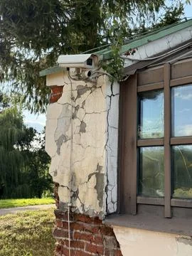Security camera mounted on weathered building corner amidst greenery and cr.. Stock Photos