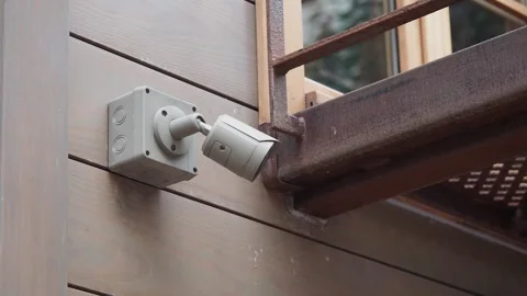 Security camera mounted on a wooden wall next to a metal railing footage. Stockbeeldmateriaal 332887620