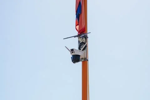 Security camera on pole with flag against clear blue sky 库存照片