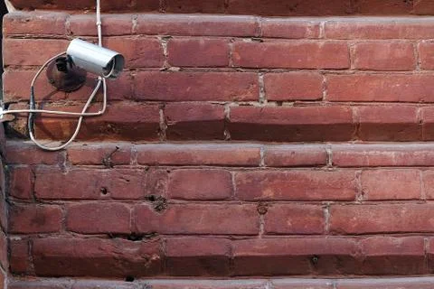 Security camera on a red brick wall. Street CCTV system. Stock Photos