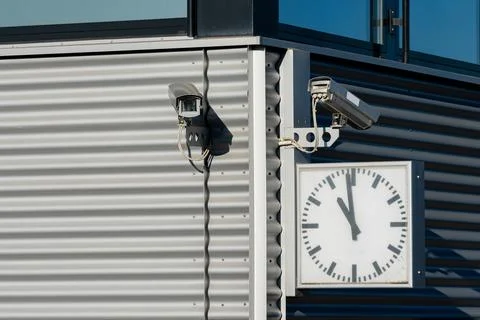 Security cameras and clock mounted on modern building exterior 스톡 사진