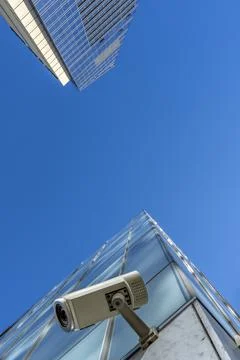 Security CCTV camera mounted on modern glass skyscraper against clear blue sk Стоковые фото