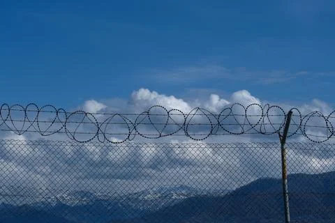 Security concept - barbed wire fence with blue sky and clouds Stock Photos