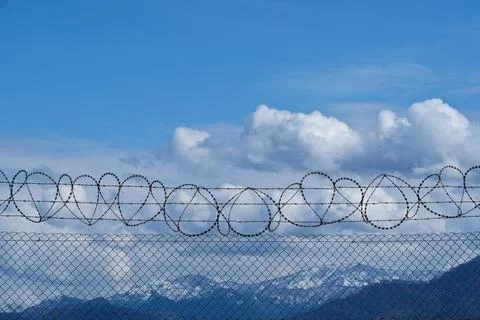 Security concept - barbed wire fence with blue sky and clouds Stock Photos