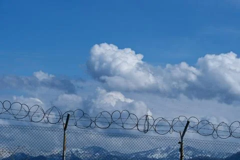Security concept - barbed wire fence with blue sky and clouds Stock Photos