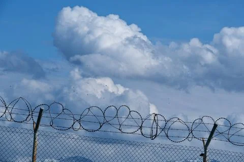 Security concept - barbed wire fence with blue sky and clouds Stock Photos