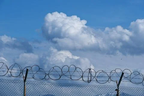 Security concept - barbed wire fence with blue sky and clouds Stock Photos