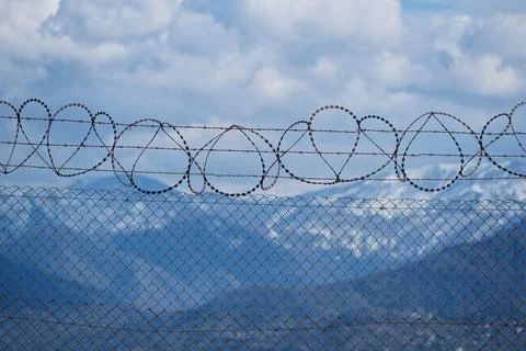 Security concept - barbed wire fence with blue sky and clouds Stock Photos