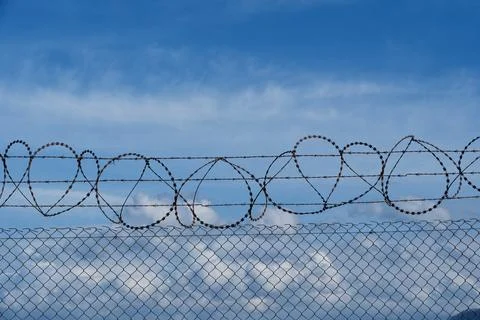 Security concept - barbed wire fence with blue sky and clouds Stock Photos