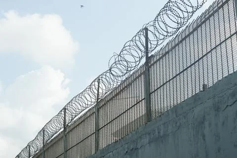 Security fence with razor wire under cloudy sky Stock Photos